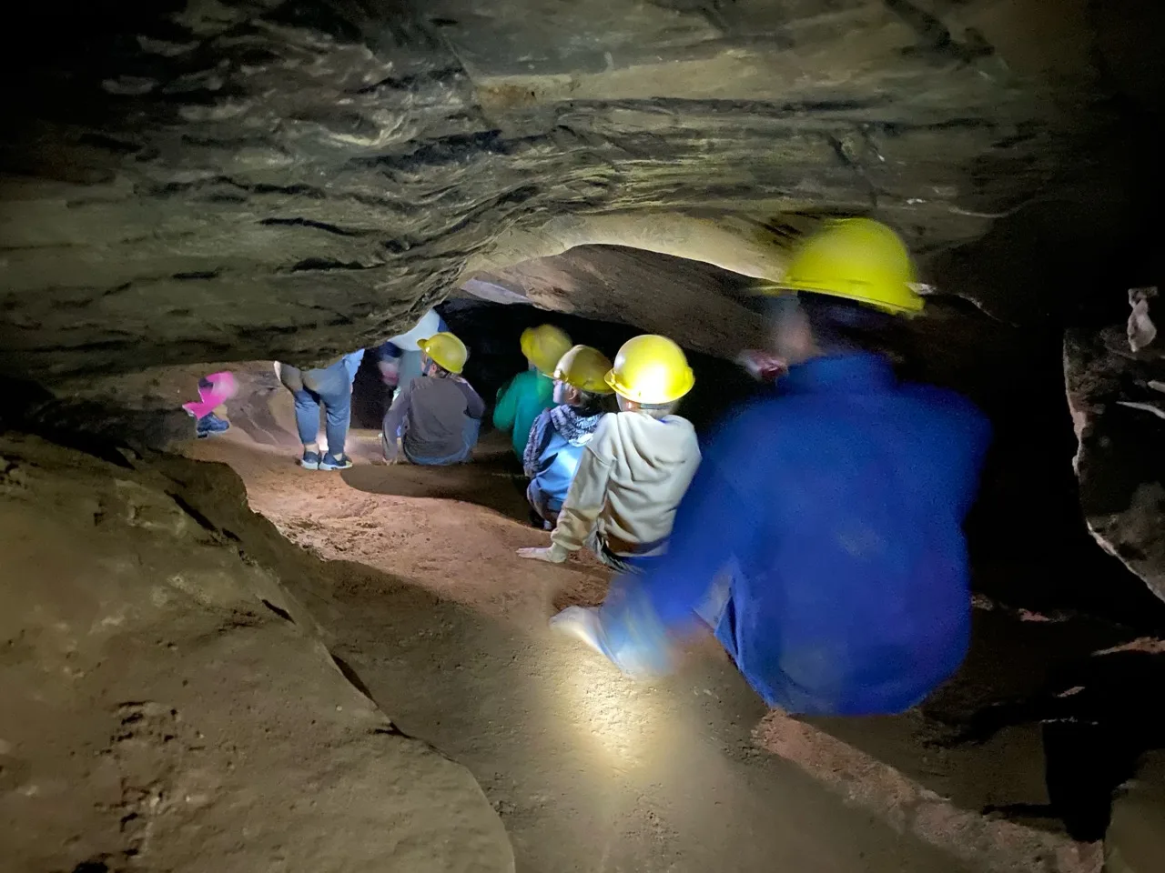 Scouts in yellow helmets moving through a low cave passage