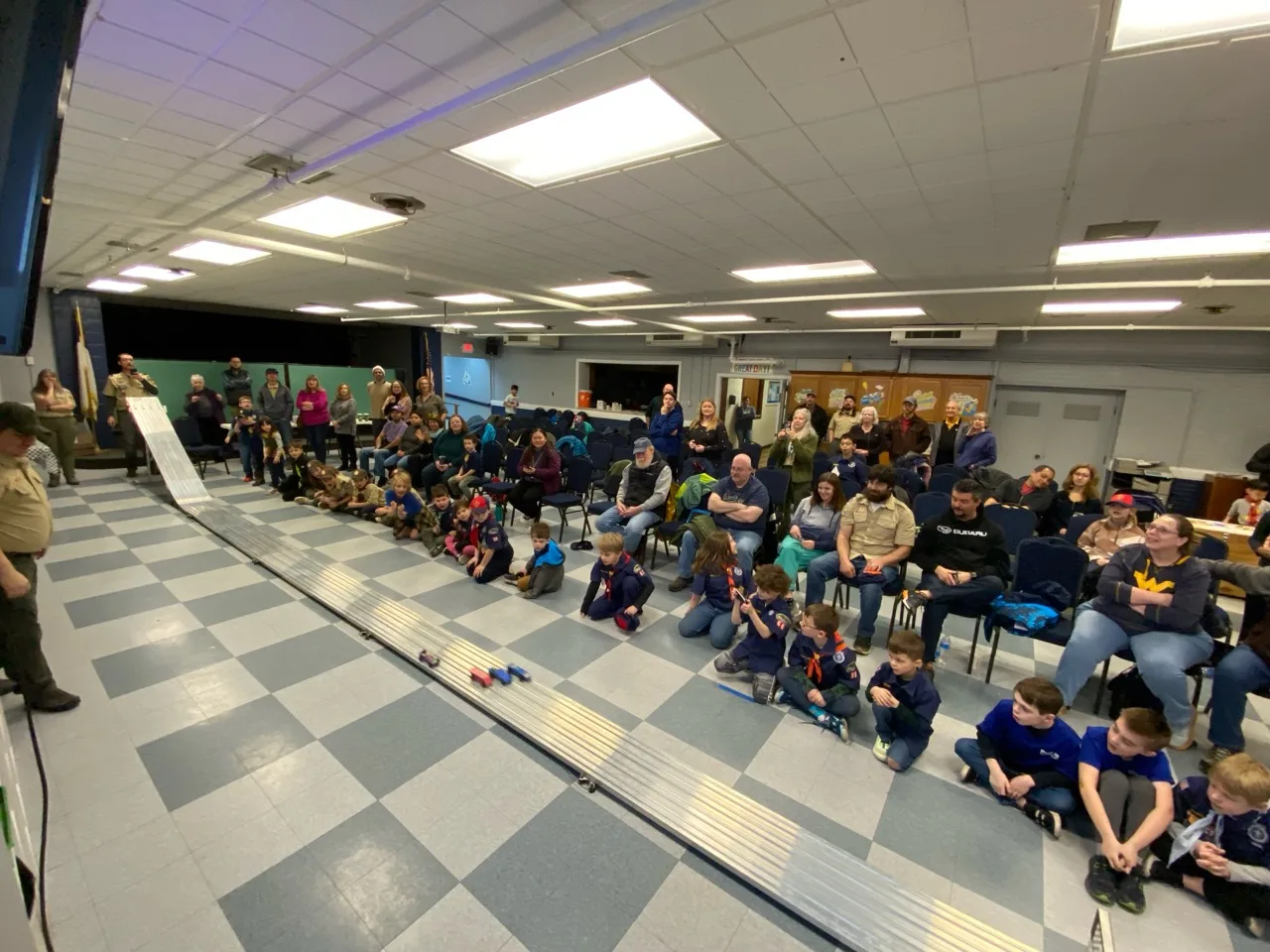 Scouts and families watching Pinewood Derby cars race down the Pack 60 track