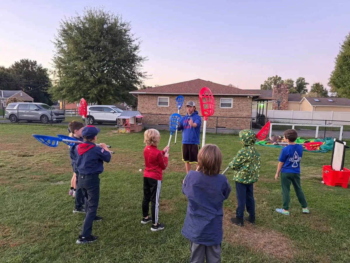 Scouts listening to a lacrosse demonstration with their sticks ready